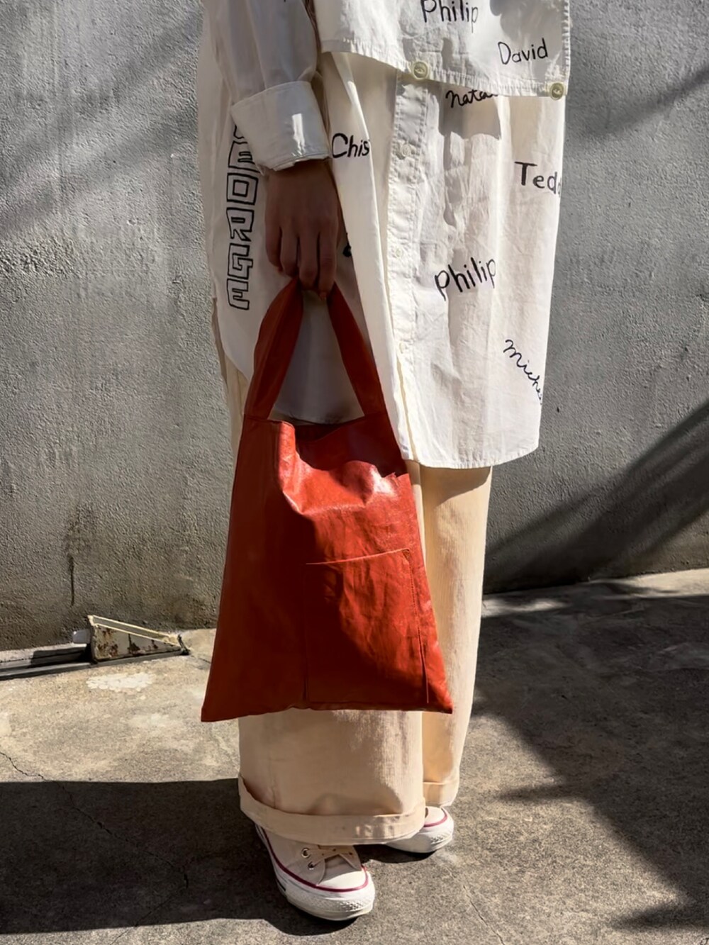 オレンジ系のトートバッグ、ホワイト系のベスト、ホワイト系のワンピースを着用したレディースの秋コーディネートの3枚目の写真