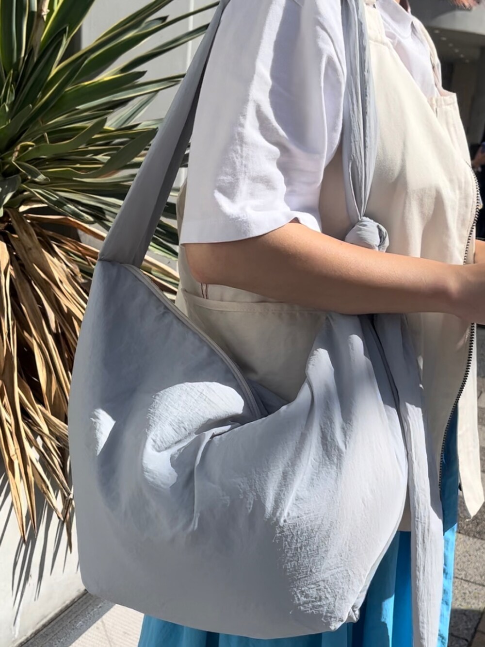 ブルー系のショルダーバッグ、ホワイト系のベスト、ブルー系のスカートを着用したレディースの夏コーディネートの2枚目の写真