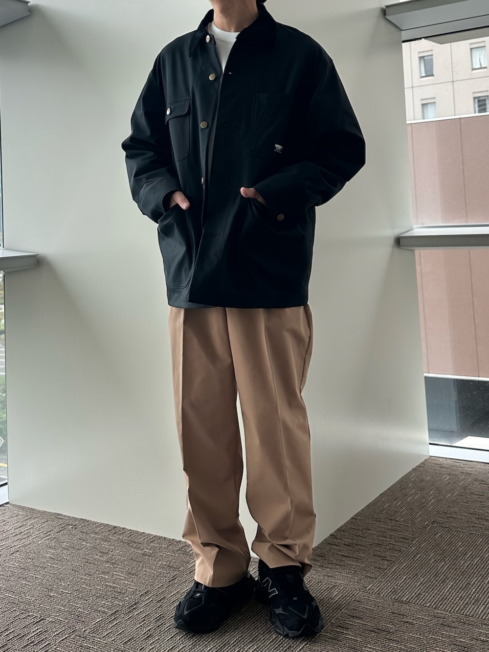 グレー系のカバーオール、ベージュ系のチノパンツ、ブラック系のスニーカーを着用したメンズの秋コーディネートの2枚目の写真