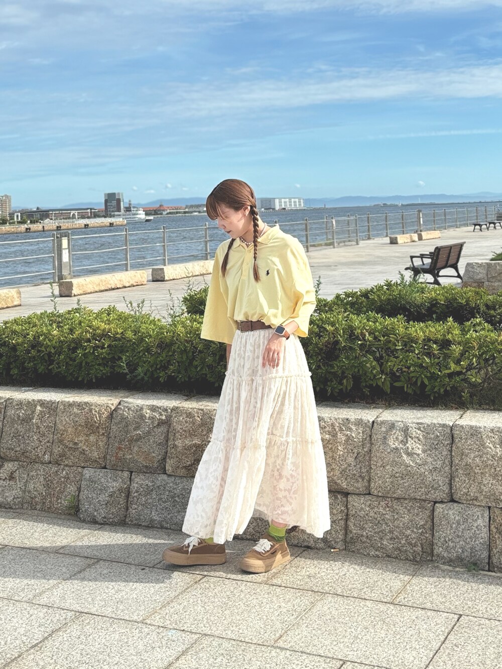 イエロー系のポロシャツ、ホワイト系のスカート、ブラウン系のスニーカーを着用したレディースの冬コーディネートの2枚目の写真