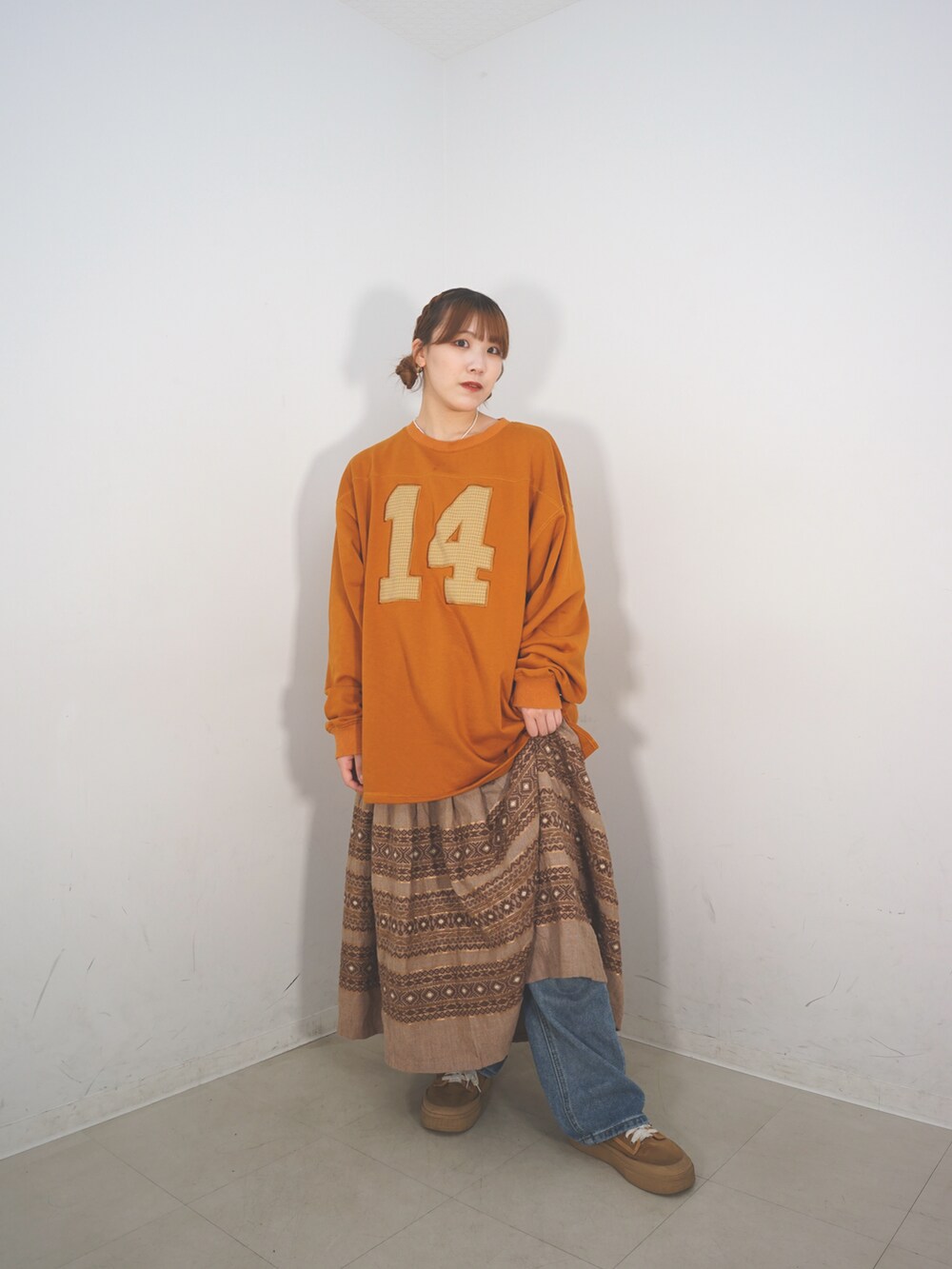 オレンジ系のスウェット、ベージュ系のスカート、ブラウン系のシューズを着用したレディースの冬コーディネートの2枚目の写真