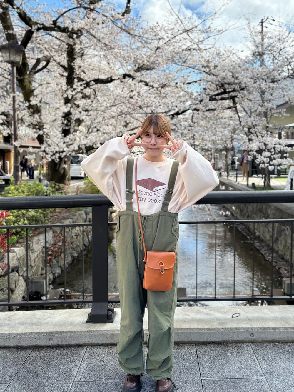 ベージュ系のスウェット、グリーン系のオールインワン・サロペット、ブラウン系のローファーを着用したレディースの春コーディネートの2枚目の写真