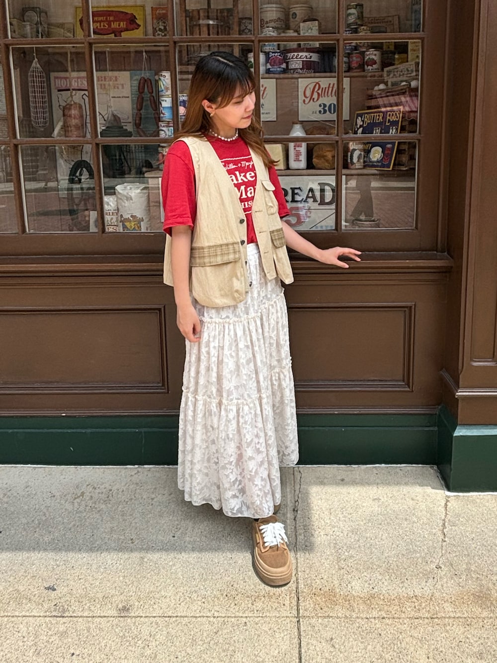 レッド系のTシャツ/カットソー、ベージュ系のベスト、ホワイト系のスカートを着用したレディースの冬コーディネートの2枚目の写真