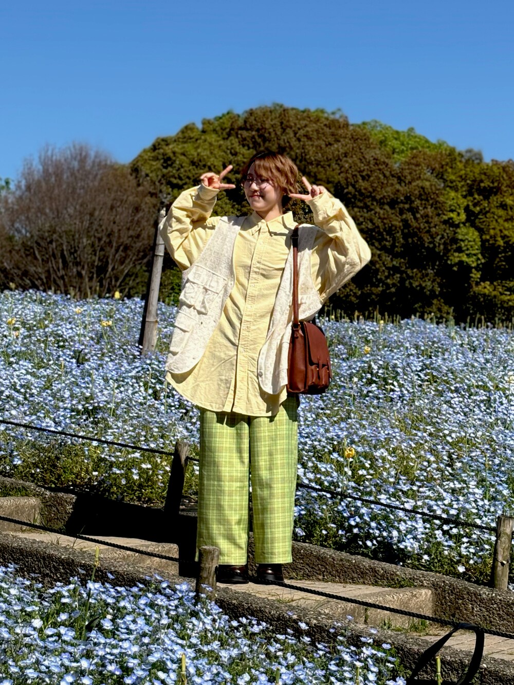 ホワイト系のベスト、グリーン系のその他パンツ、イエロー系のショルダーバッグを着用したレディースの春コーディネートの2枚目の写真