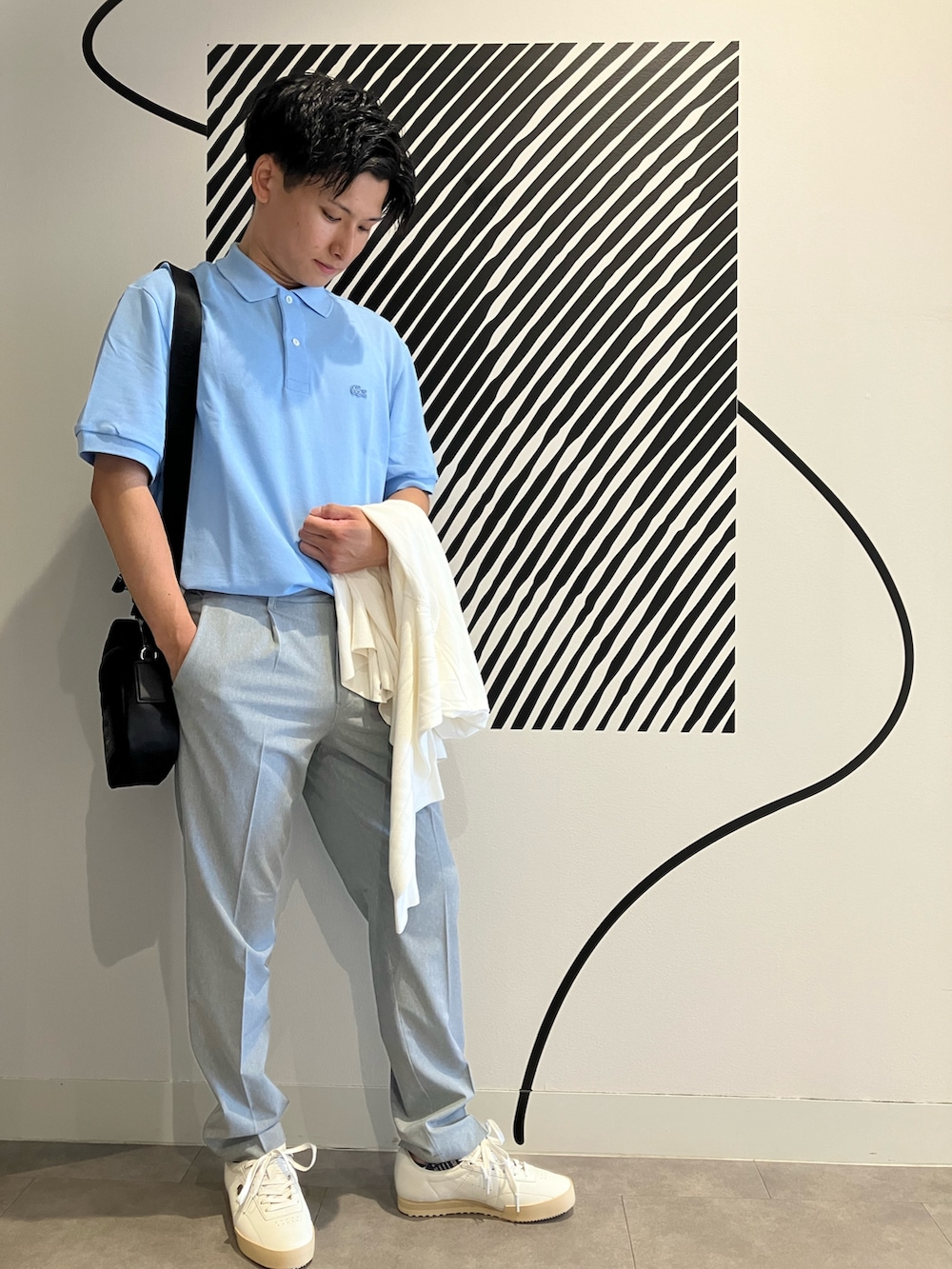 グレー系のチノパンツ、ブラック系のショルダーバッグ、ブルー系のポロシャツを着用したメンズの夏コーディネートの3枚目の写真