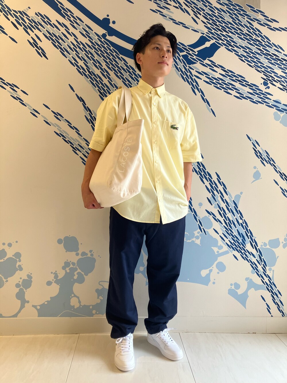 イエロー系のシャツ/ブラウス、ホワイト系のスニーカー、ブルー系のチノパンツを着用したメンズの夏コーディネートの2枚目の写真