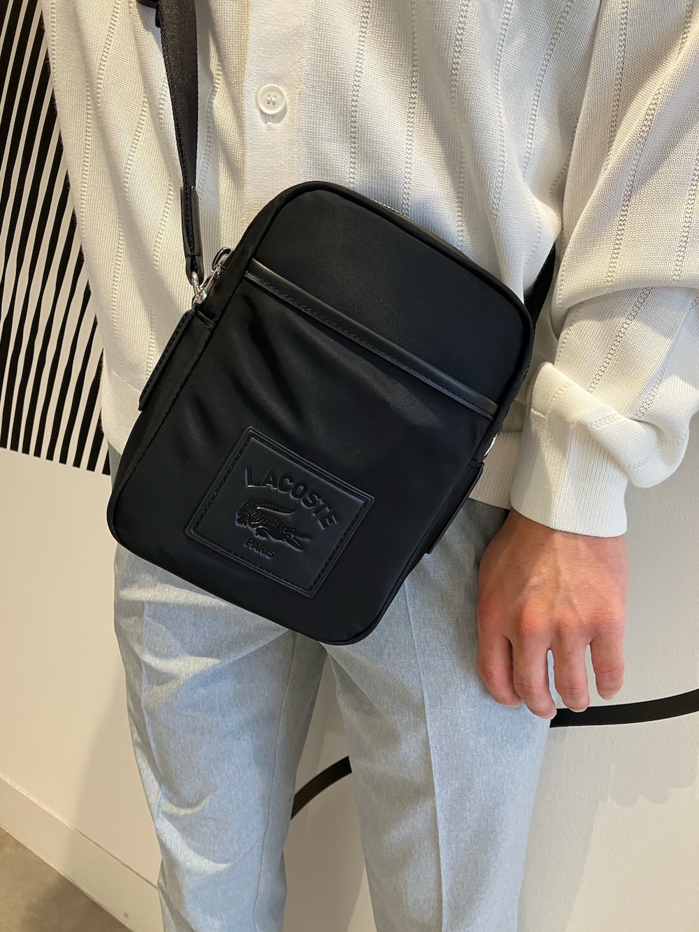 グレー系のチノパンツ、ブラック系のショルダーバッグ、ブルー系のポロシャツを着用したメンズの夏コーディネートの5枚目の写真