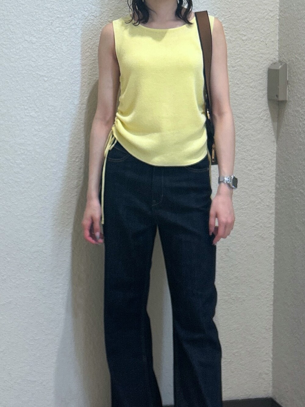 イエロー系のニット/セーター、ブルー系のデニムパンツ、ブラック系のショルダーバッグを着用したレディースの夏コーディネートの4枚目の写真