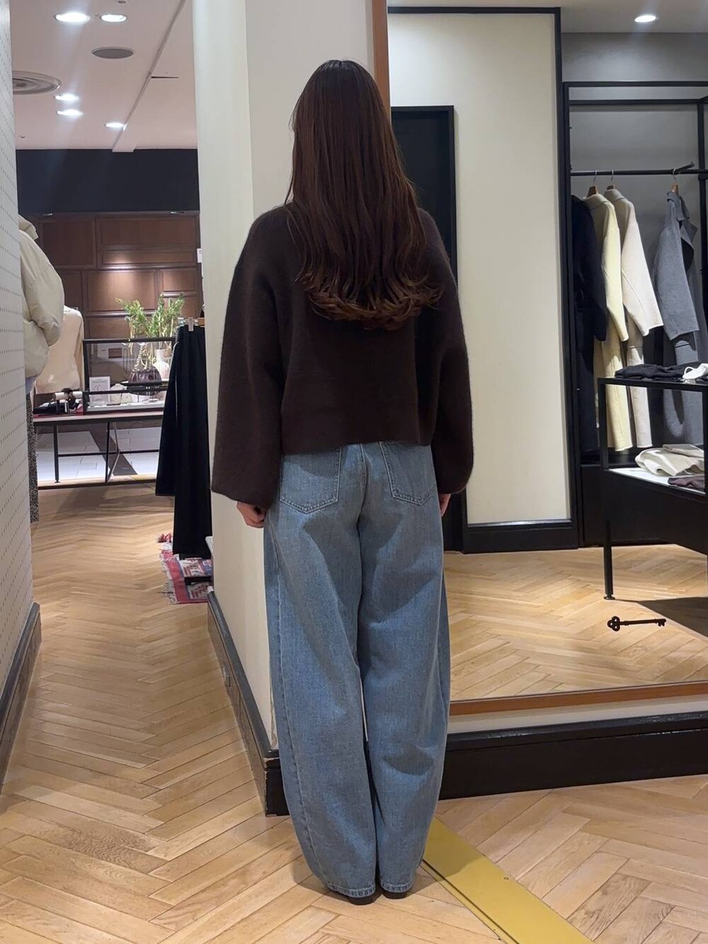 ブルー系のデニムパンツ、ブラウン系のブーツ、ベージュ系のハンドバッグを着用したレディースの冬コーディネートの3枚目の写真