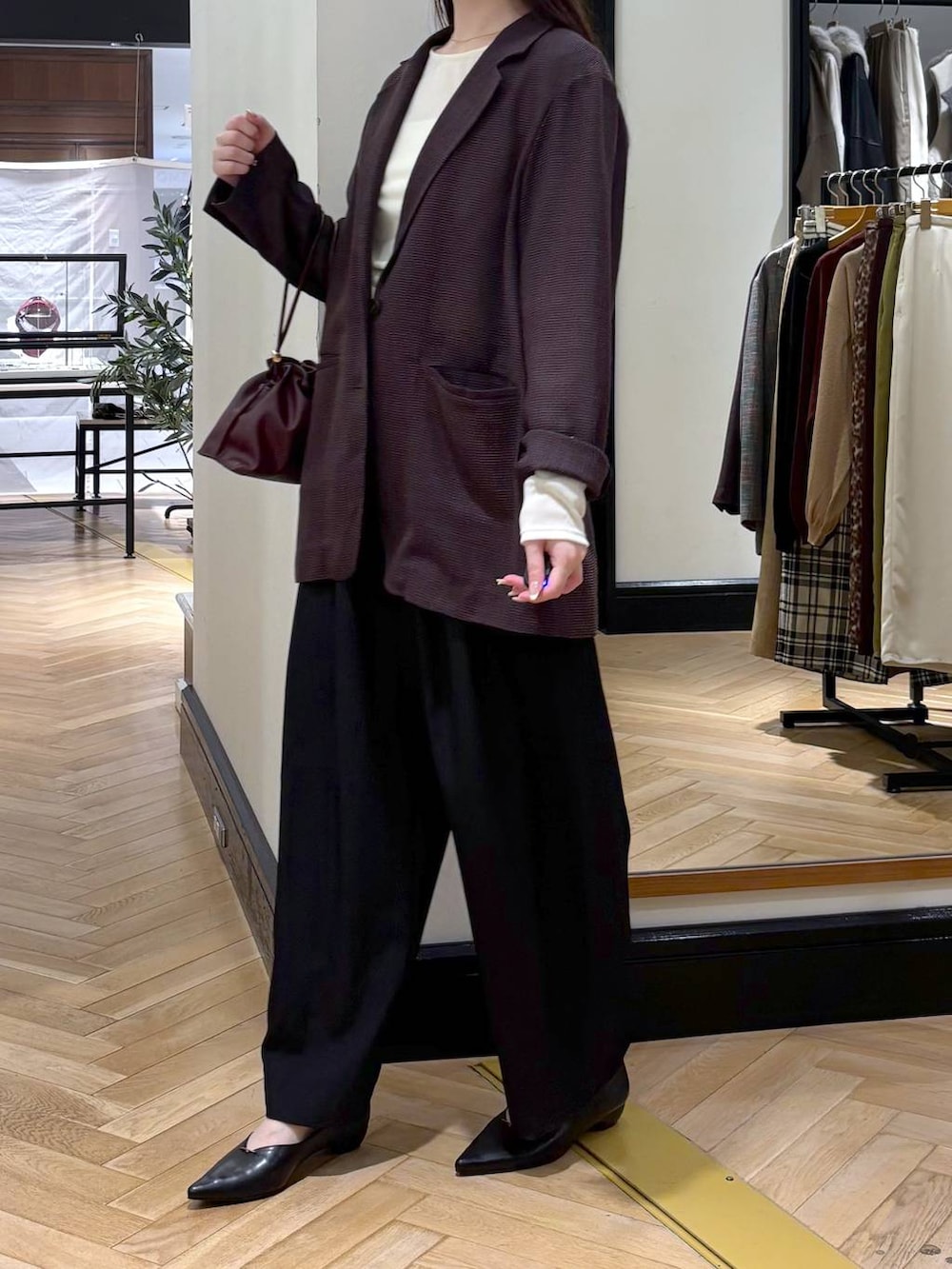 レッド系のショルダーバッグ、ブラック系のパンプス、ブラック系のスラックスを着用したレディースの秋コーディネートの3枚目の写真