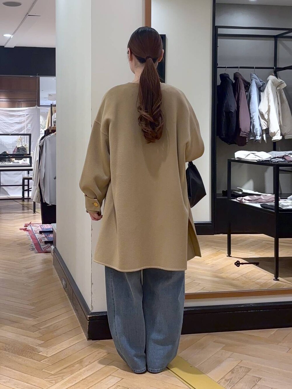 ブルー系のデニムパンツ、ベージュ系のノーカラーコート、ブラック系のショルダーバッグを着用したレディースの秋コーディネートの4枚目の写真