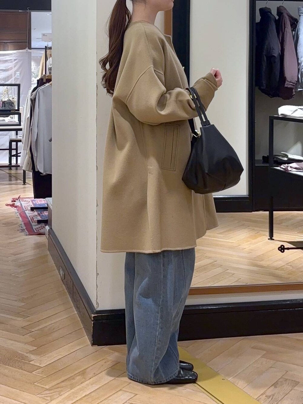 ブルー系のデニムパンツ、ベージュ系のノーカラーコート、ブラック系のショルダーバッグを着用したレディースの秋コーディネートの2枚目の写真