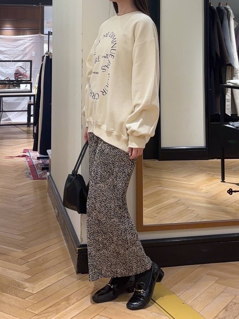 ブラック系のローファー、ベージュ系のスカート、ブラック系のショルダーバッグを着用したレディースの秋コーディネートの3枚目の写真