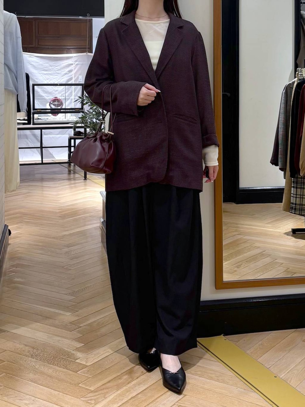 レッド系のショルダーバッグ、ブラック系のパンプス、ブラック系のスラックスを着用したレディースの秋コーディネートの2枚目の写真