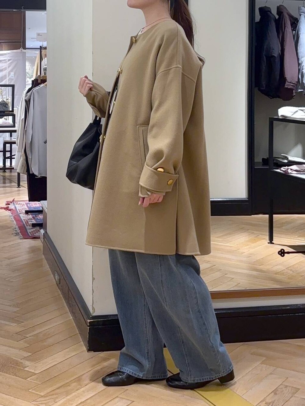 ブルー系のデニムパンツ、ベージュ系のノーカラーコート、ブラック系のショルダーバッグを着用したレディースの秋コーディネートの3枚目の写真
