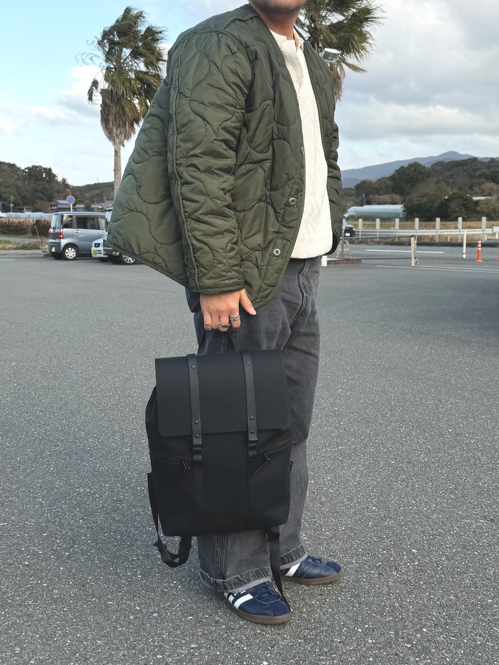 グリーン系のミリタリージャケット、ブラック系のバックパック/リュック、グレー系のデニムパンツを着用したメンズの春コーディネートの2枚目の写真