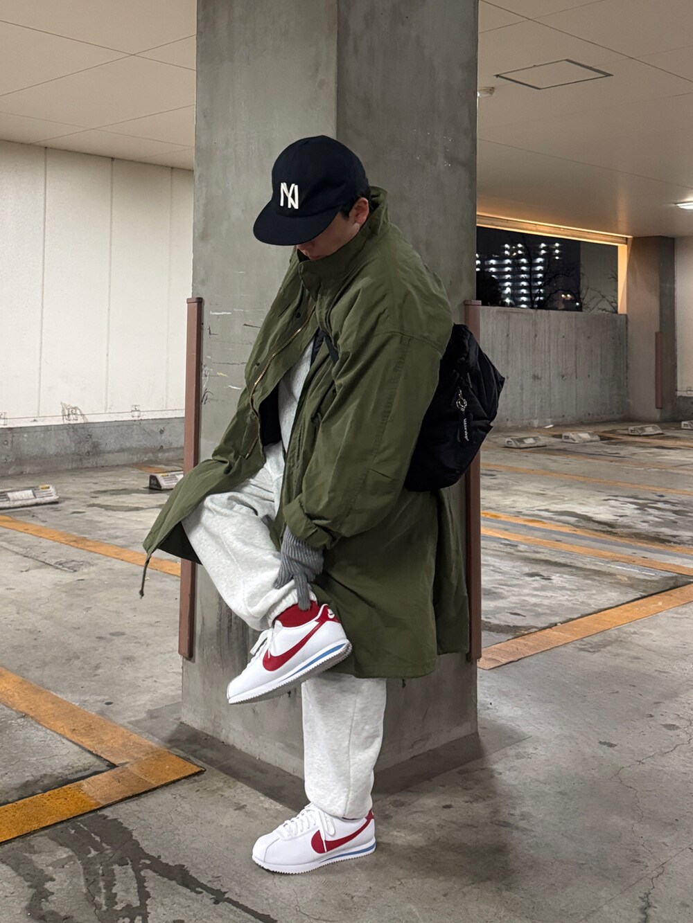 ブラック系のショルダーバッグ、グリーン系のモッズコート、ホワイト系のスウェットパンツを着用したメンズの春コーディネートの2枚目の写真
