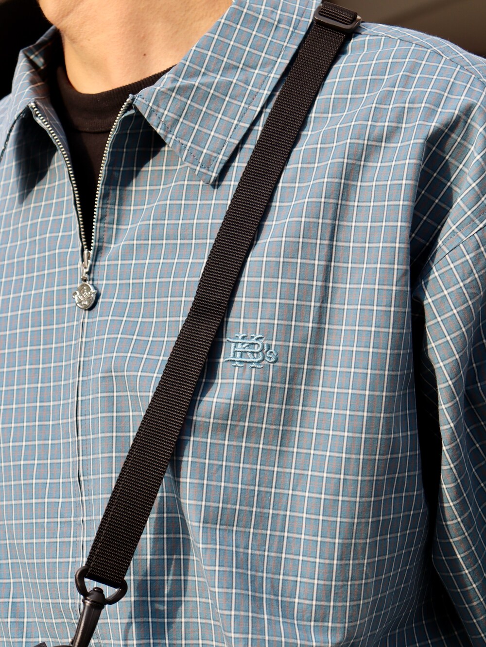 ブルー系のブルゾン、ブラック系のショルダーバッグ、ブラック系のデニムパンツを着用したメンズの春コーディネートの3枚目の写真