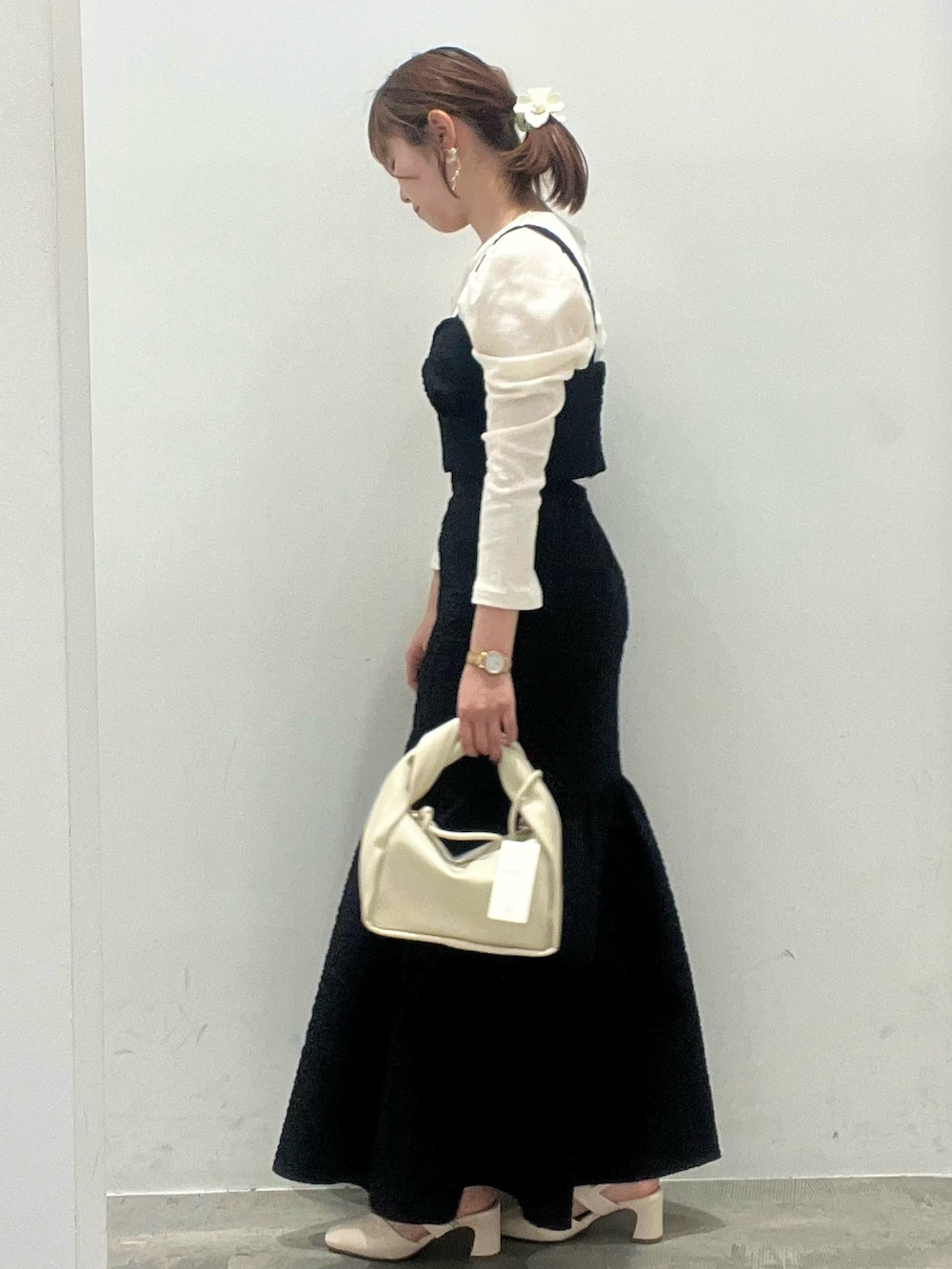 ブラック系のスカート、ブラック系のベスト、ホワイト系のショルダーバッグを着用したレディースの春コーディネートの3枚目の写真