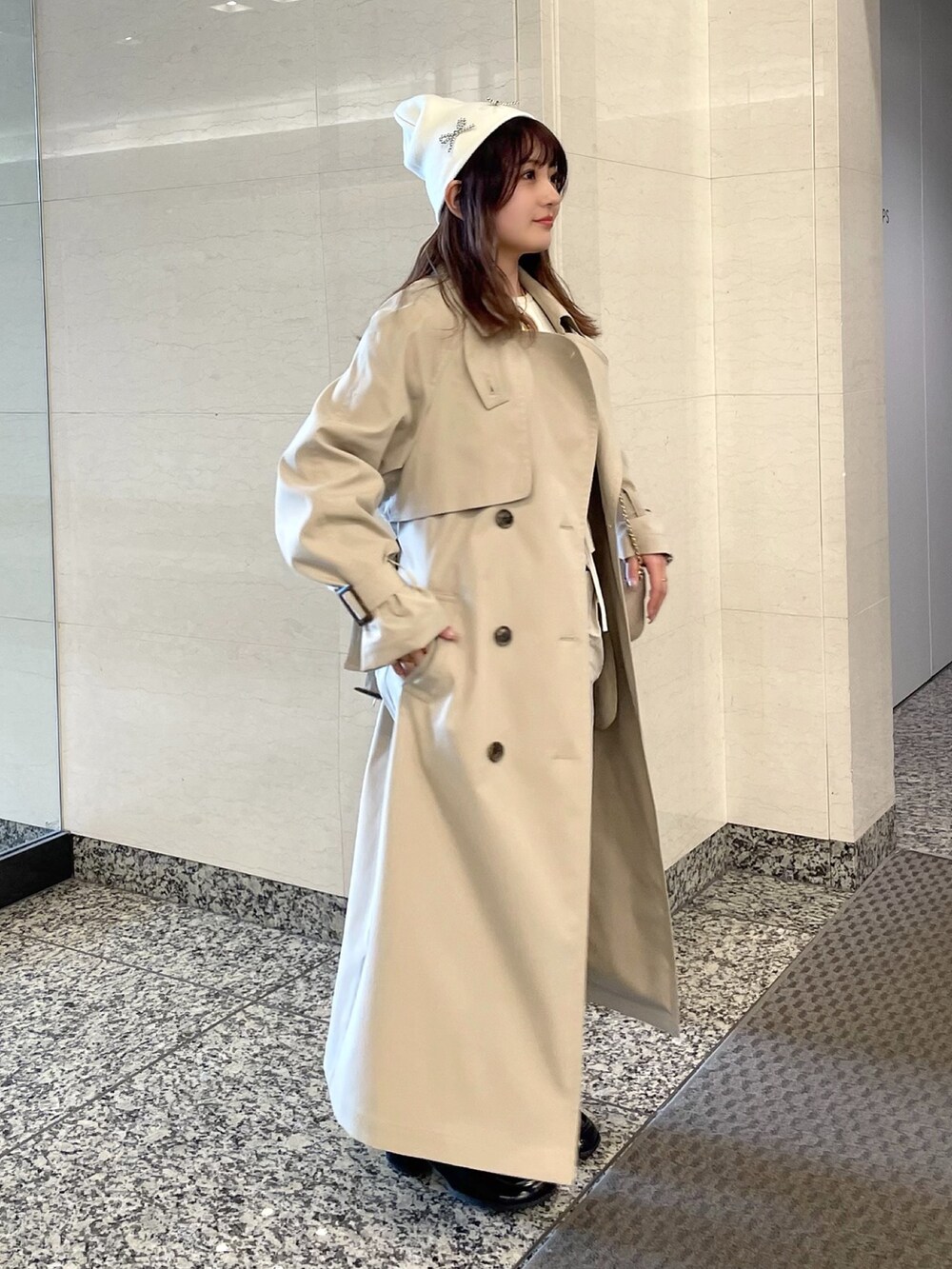 ベージュ系のトレンチコート、ホワイト系のニット/セーター、ベージュ系のショルダーバッグを着用したレディースの春コーディネートの2枚目の写真