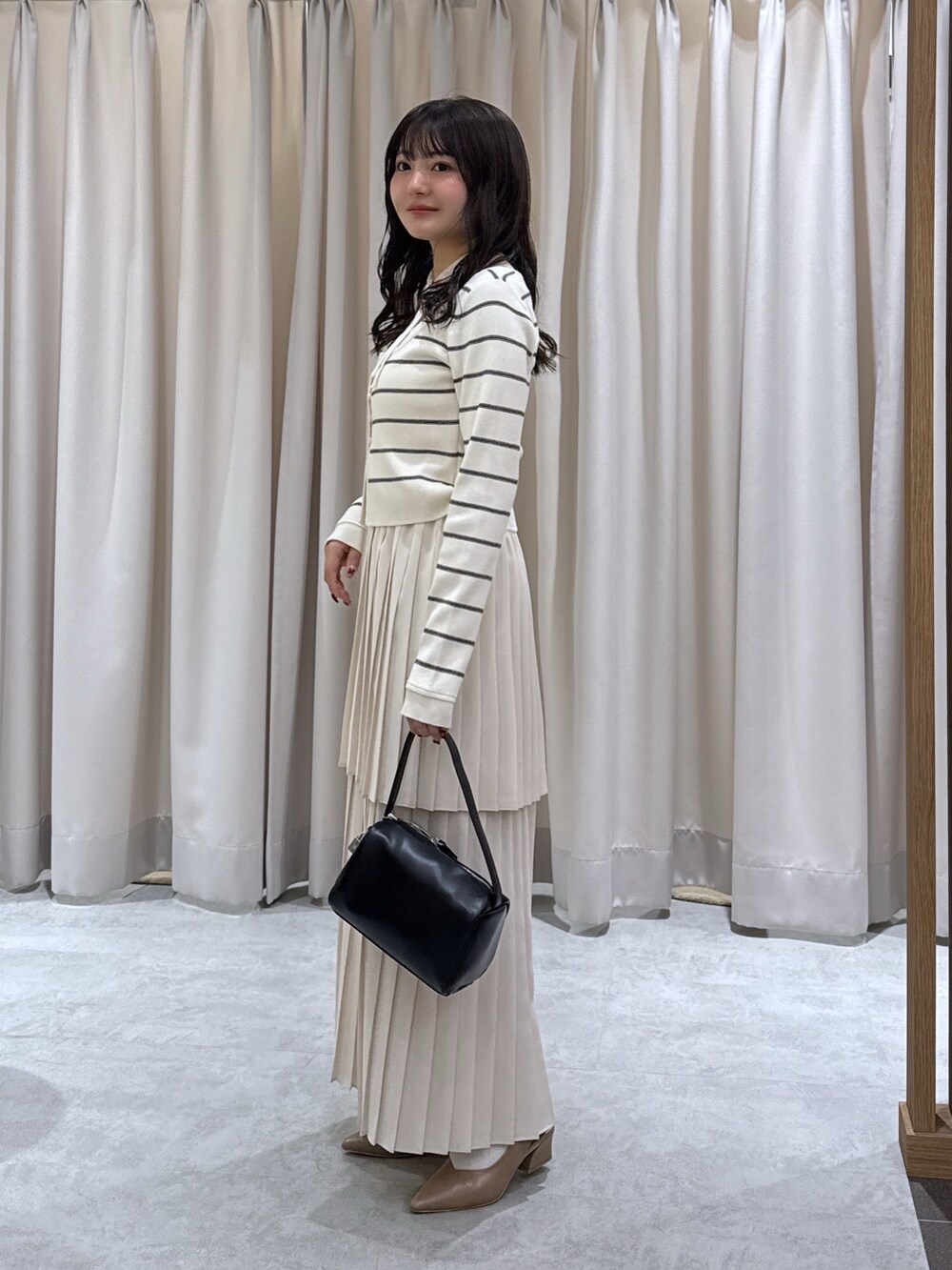 ホワイト系のニット/セーター、ホワイト系のスカート、ブラック系のハンドバッグを着用したレディースの春コーディネートの2枚目の写真
