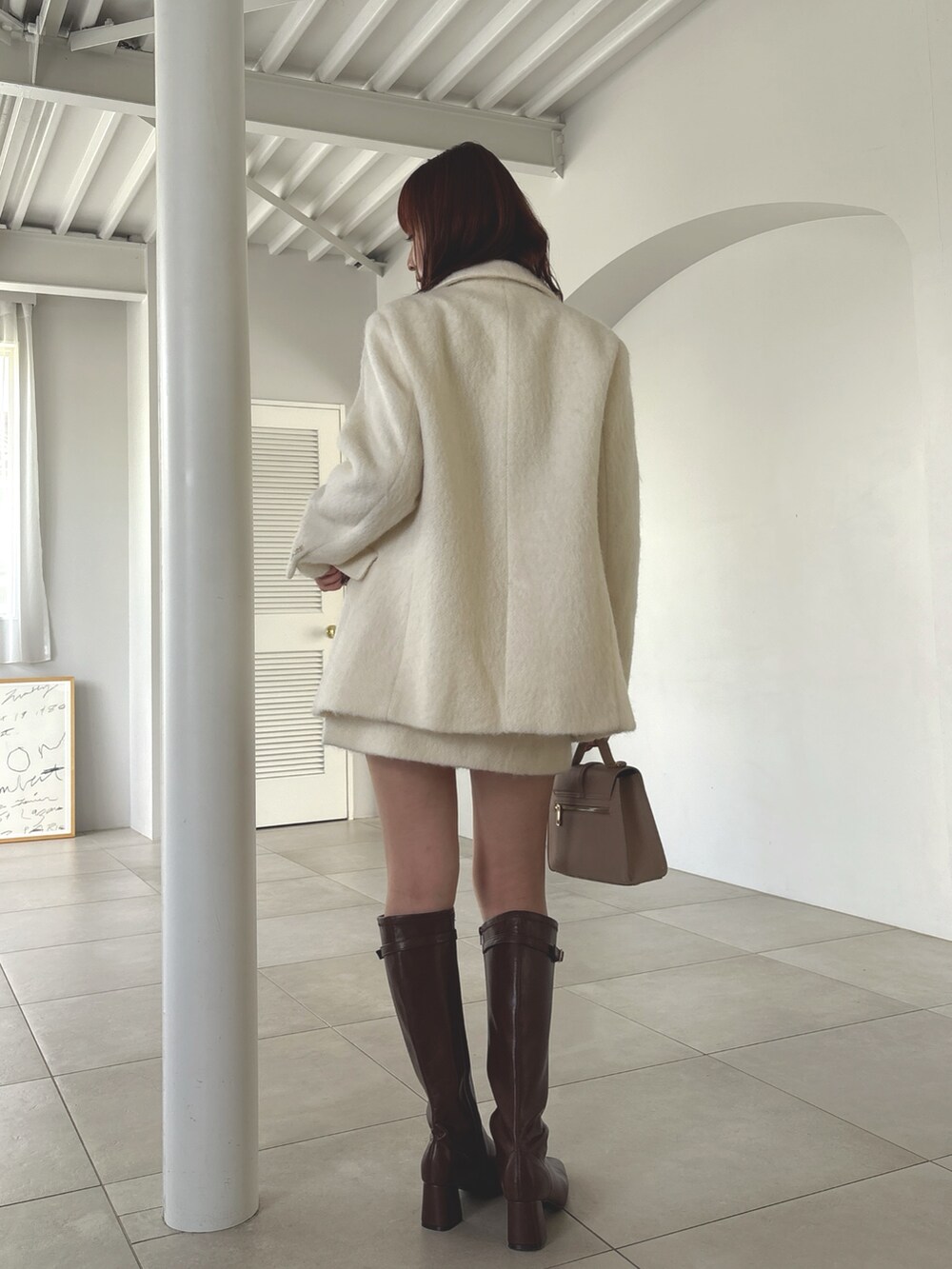 ホワイト系のテーラードジャケット、ホワイト系のスカート、ブラウン系のブーツを着用したレディースの夏コーディネートの3枚目の写真