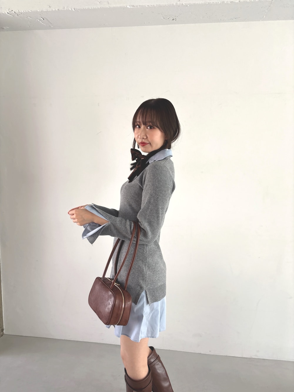 グレー系のワンピース、ブラウン系のハンドバッグ、ブラウン系のブーツを着用したレディースの秋コーディネートの7枚目の写真