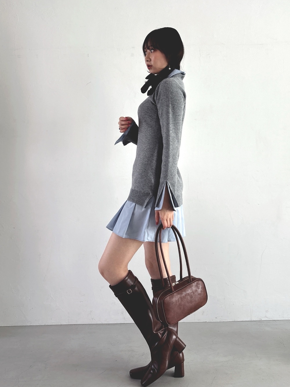 グレー系のワンピース、ブラウン系のハンドバッグ、ブラウン系のブーツを着用したレディースの秋コーディネートの3枚目の写真
