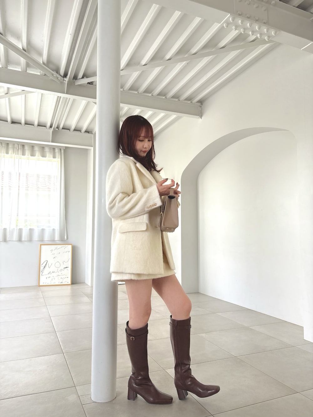 ホワイト系のテーラードジャケット、ホワイト系のスカート、ブラウン系のブーツを着用したレディースの夏コーディネートの4枚目の写真