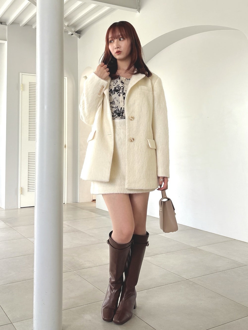 ホワイト系のテーラードジャケット、ホワイト系のスカート、ブラウン系のブーツを着用したレディースの夏コーディネートの2枚目の写真