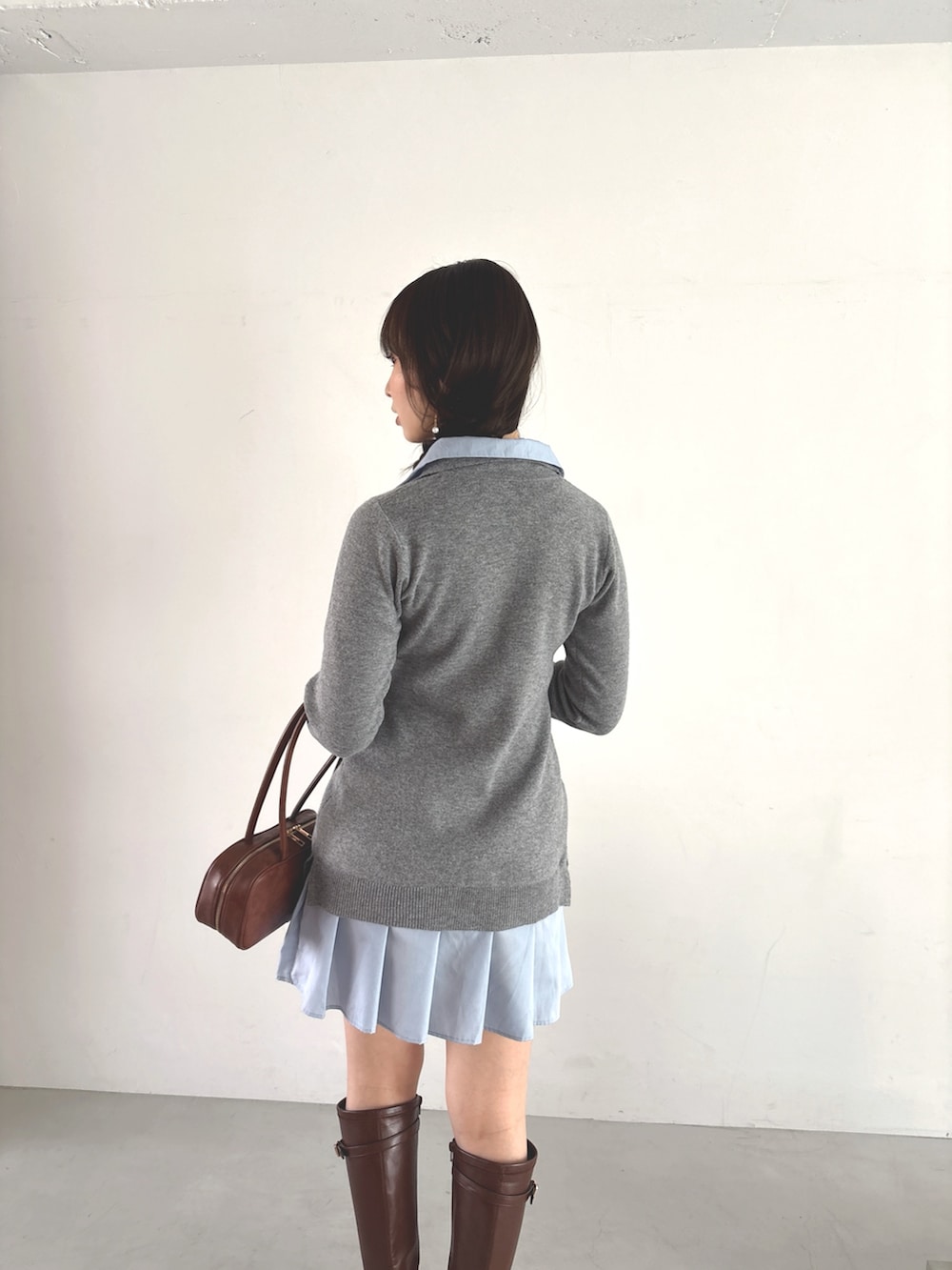 グレー系のワンピース、ブラウン系のハンドバッグ、ブラウン系のブーツを着用したレディースの秋コーディネートの6枚目の写真