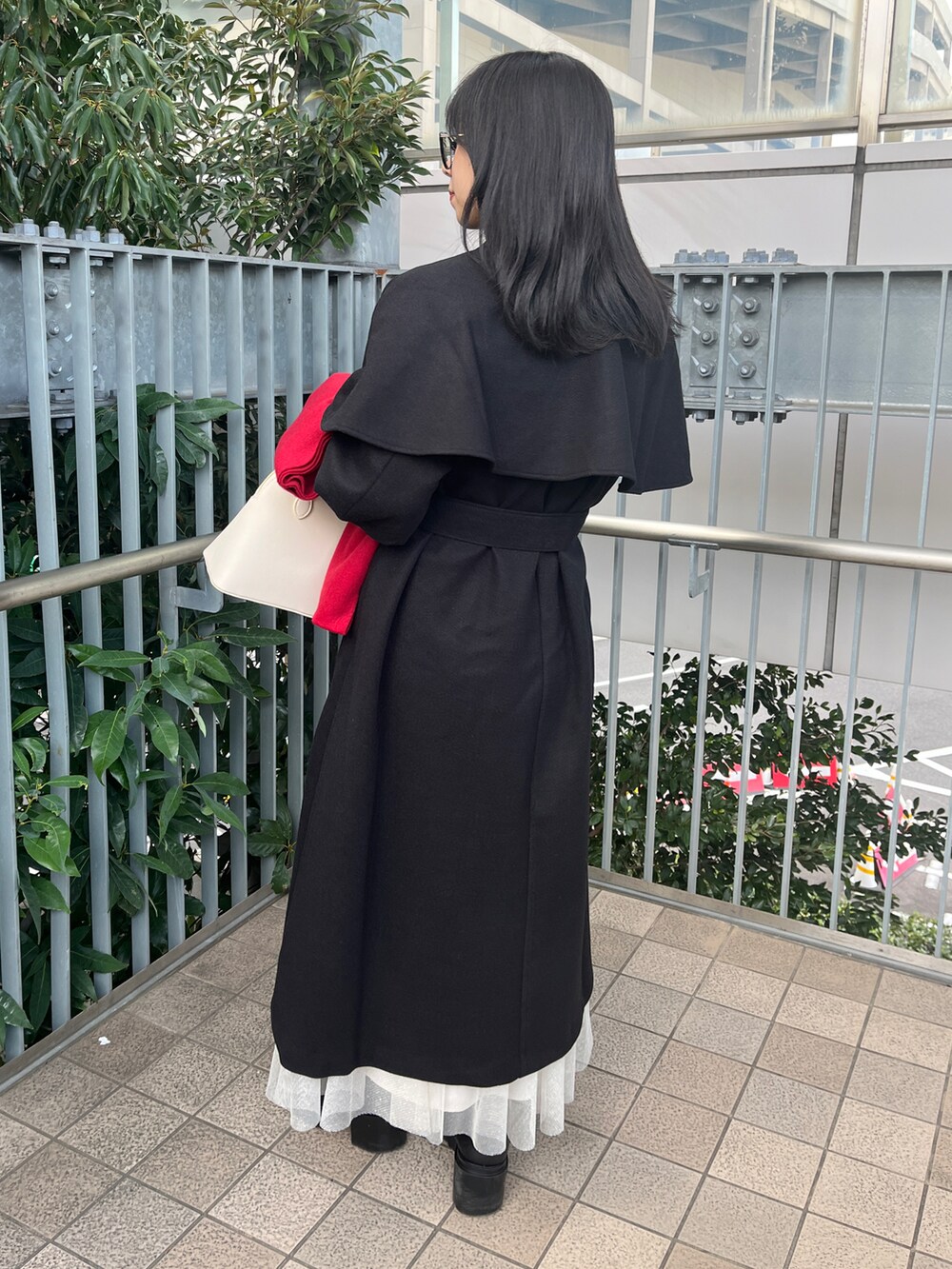 ブラック系のステンカラーコート、ホワイト系のハンドバッグ、レッド系のファッション雑貨を着用したレディースの秋コーディネートの2枚目の写真