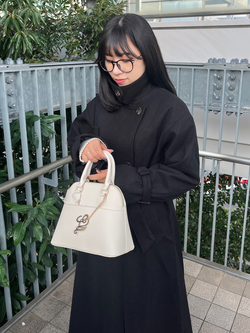 ブラック系のステンカラーコート、ホワイト系のハンドバッグ、レッド系のファッション雑貨を着用したレディースの秋コーディネートの3枚目の写真