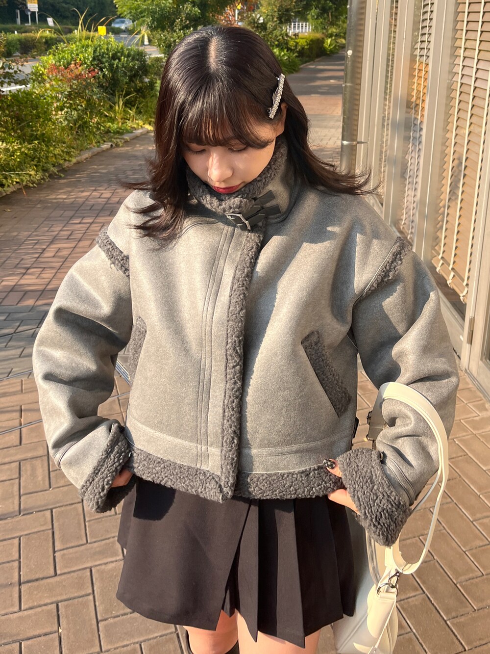 グレー系のムートンコート、ブラック系のパンツ、ホワイト系のショルダーバッグを着用したレディースの冬コーディネートの2枚目の写真