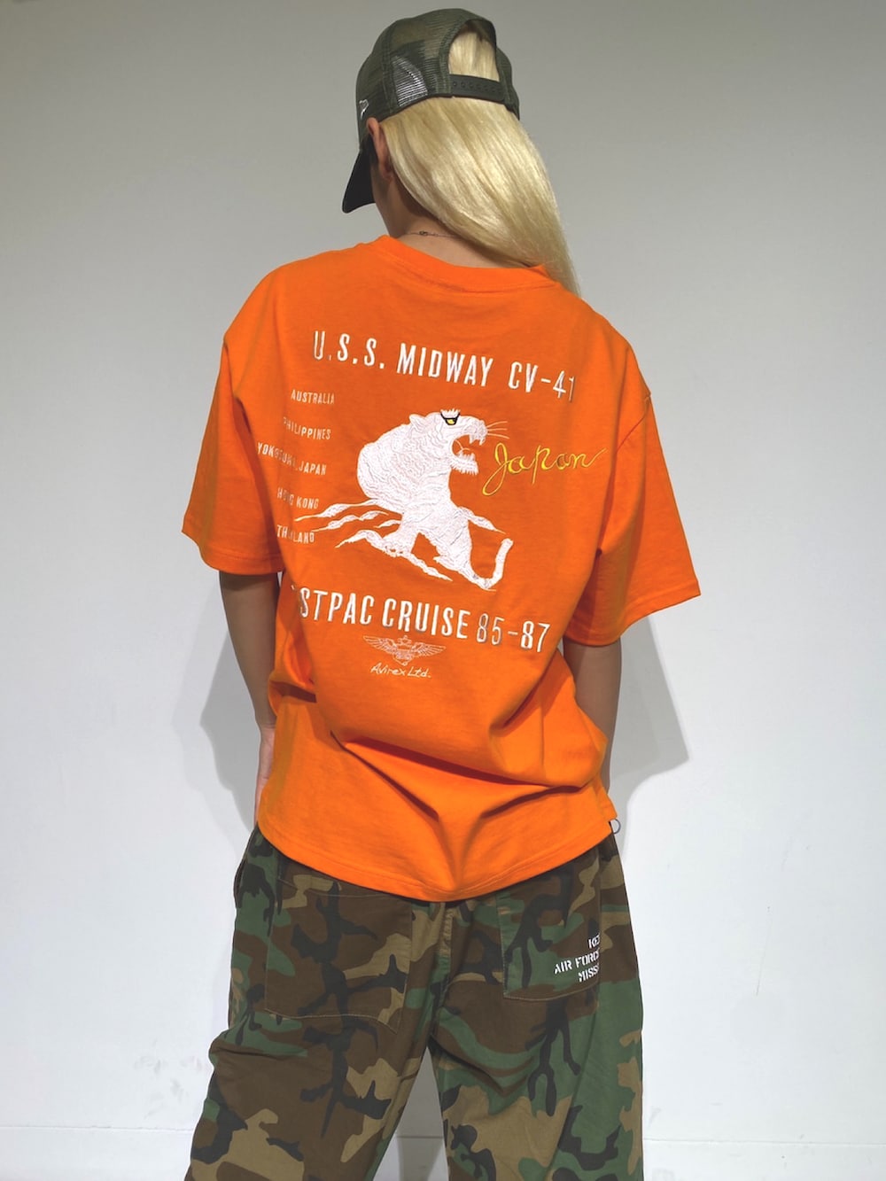 オレンジ系のTシャツ/カットソー、ベージュ系のキャップを着用したレディースの夏コーディネートの2枚目の写真