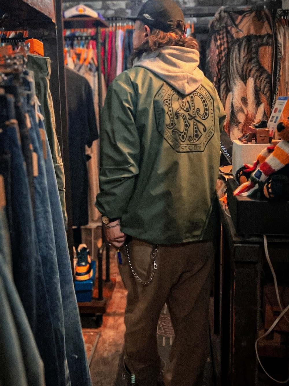 グリーン系のトップス、ベージュ系のチノパンツ、グレー系のパーカーを着用したメンズの春コーディネートの2枚目の写真