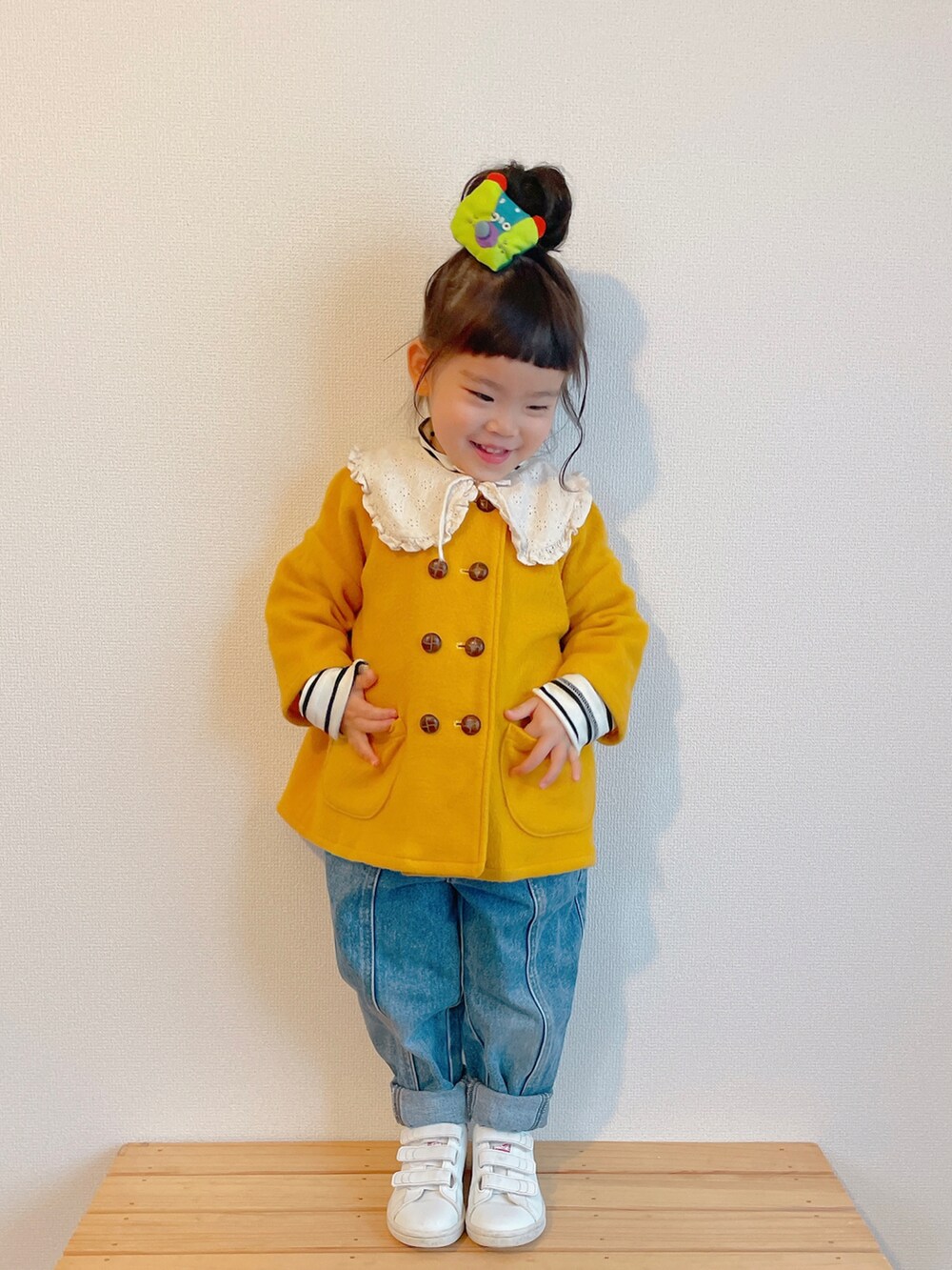 イエロー系のノーカラーコート、ブルー系のデニムパンツ、ホワイト系のスニーカーを着用したキッズの冬コーディネートの2枚目の写真