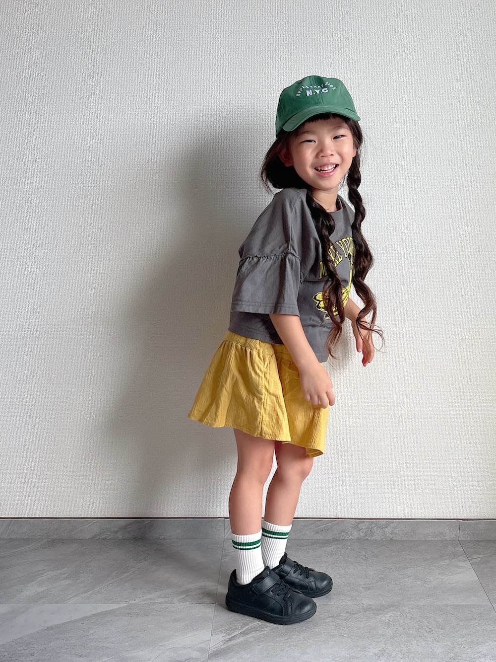 ブラック系のスニーカー、グレー系のTシャツ/カットソー、イエロー系のスカートを着用したキッズの夏コーディネートの2枚目の写真