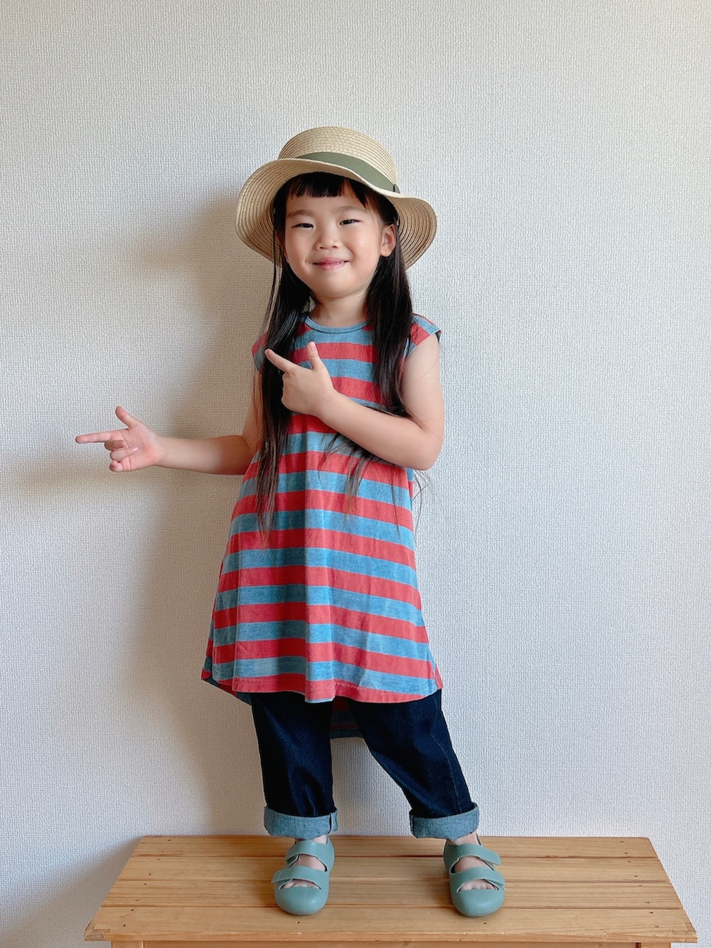 レッド系のワンピース、ベージュ系のデニムパンツ、グリーン系のサンダルを着用したキッズの夏コーディネートの2枚目の写真