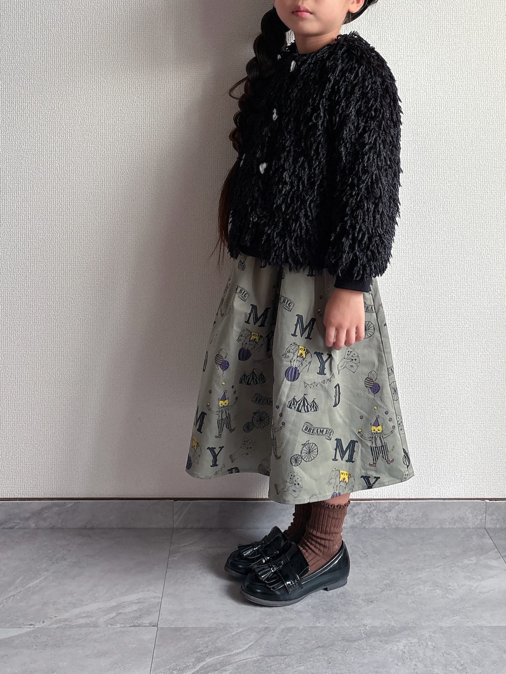 ブラック系のカーディガン/ボレロ、グリーン系のスカートを着用したキッズの秋コーディネートの2枚目の写真