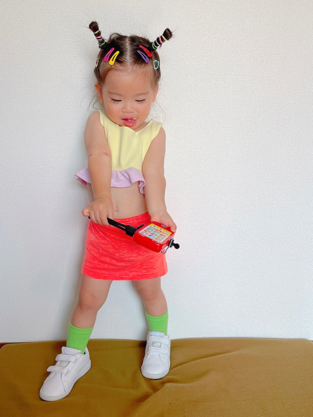 ピンク系のスカート、ホワイト系のスニーカー、イエロー系のスポーツブラを着用したキッズの秋コーディネートの2枚目の写真