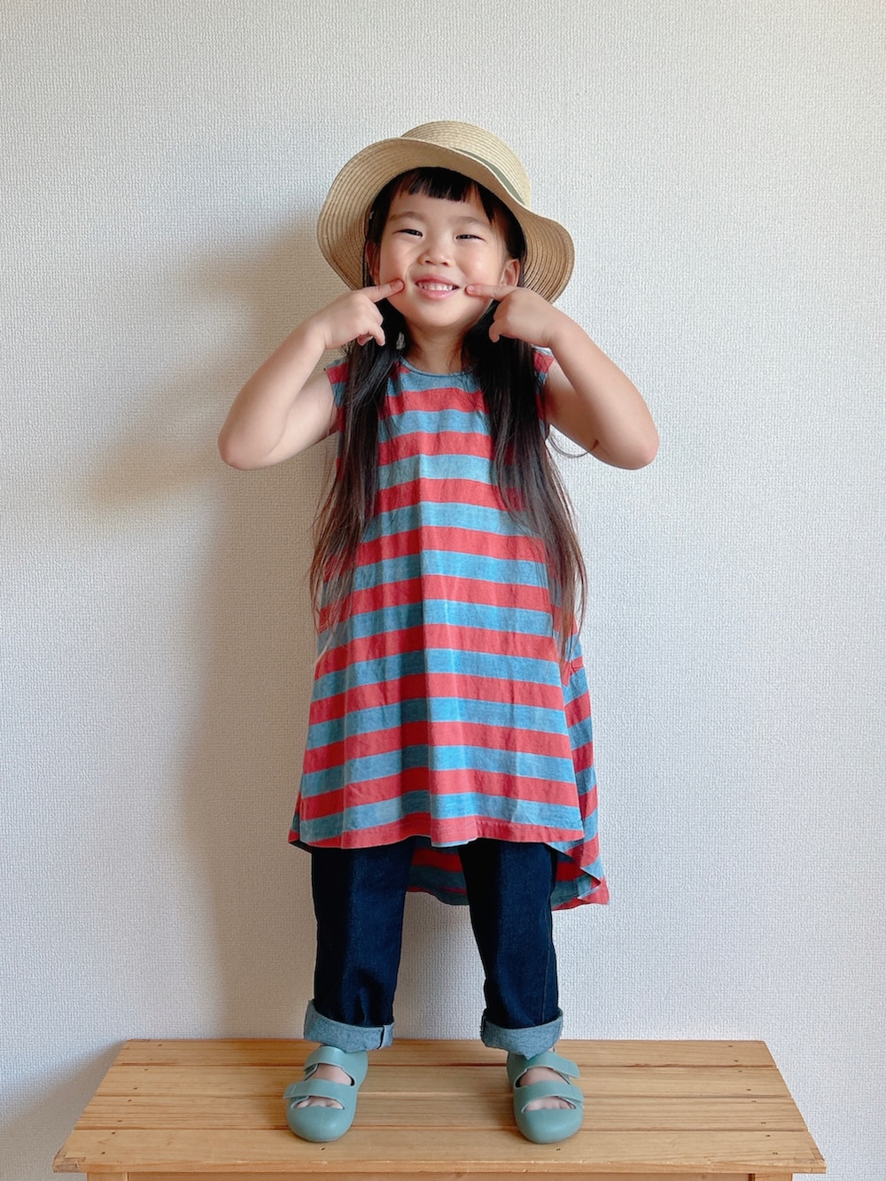 レッド系のワンピース、ベージュ系のデニムパンツ、グリーン系のサンダルを着用したキッズの夏コーディネートの3枚目の写真