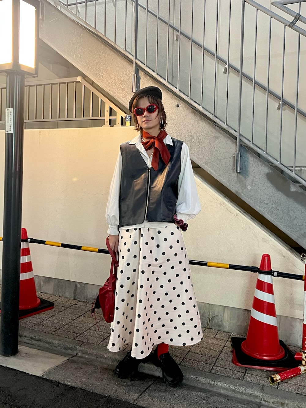 レッド系のショルダーバッグ、ブラック系のベスト、ブラック系のハンチング/ベレー帽を着用したメンズの秋コーディネートの2枚目の写真