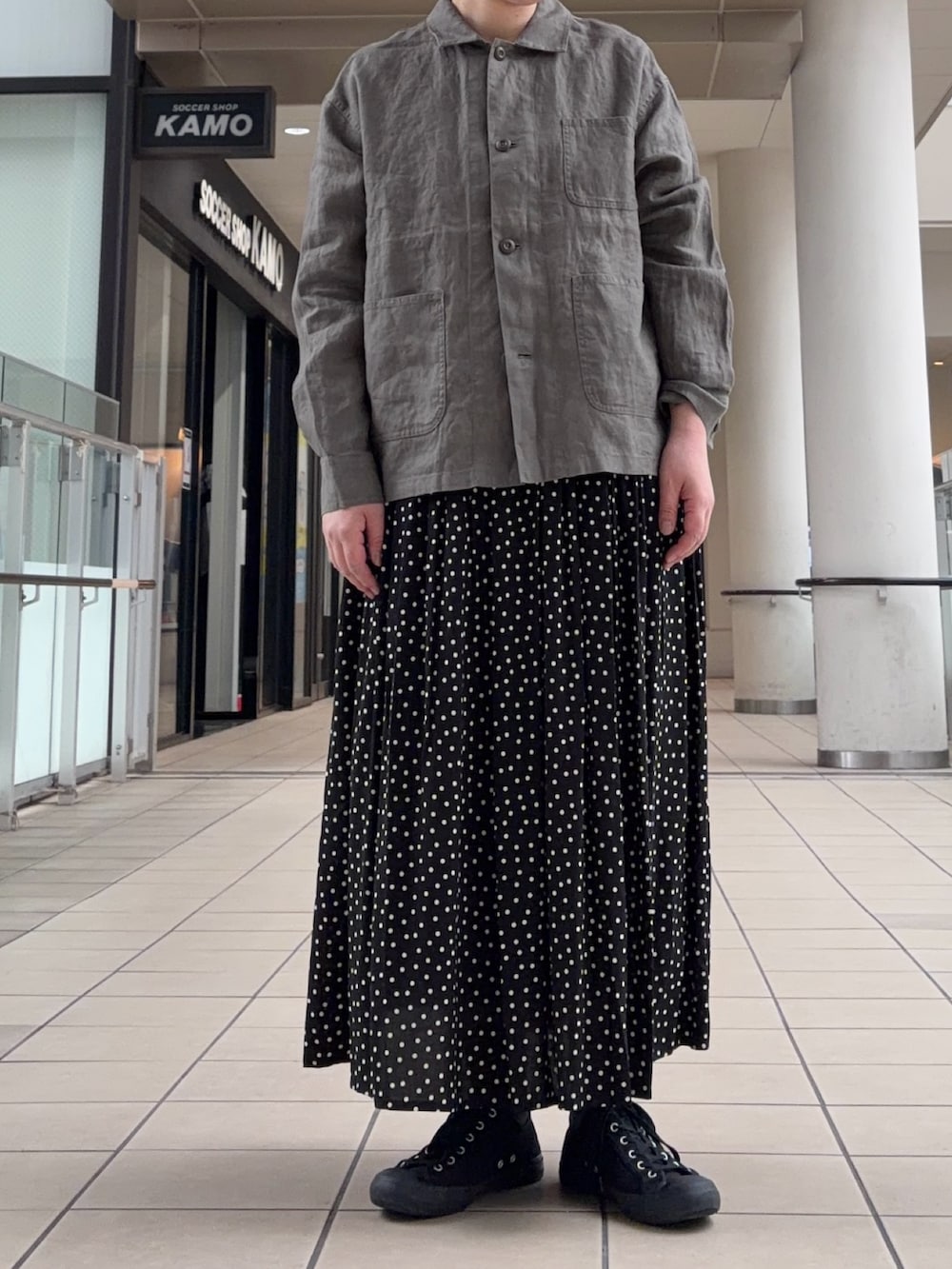 グレー系のカバーオール、ブラック系のスカートを着用したレディースの春コーディネートの2枚目の写真