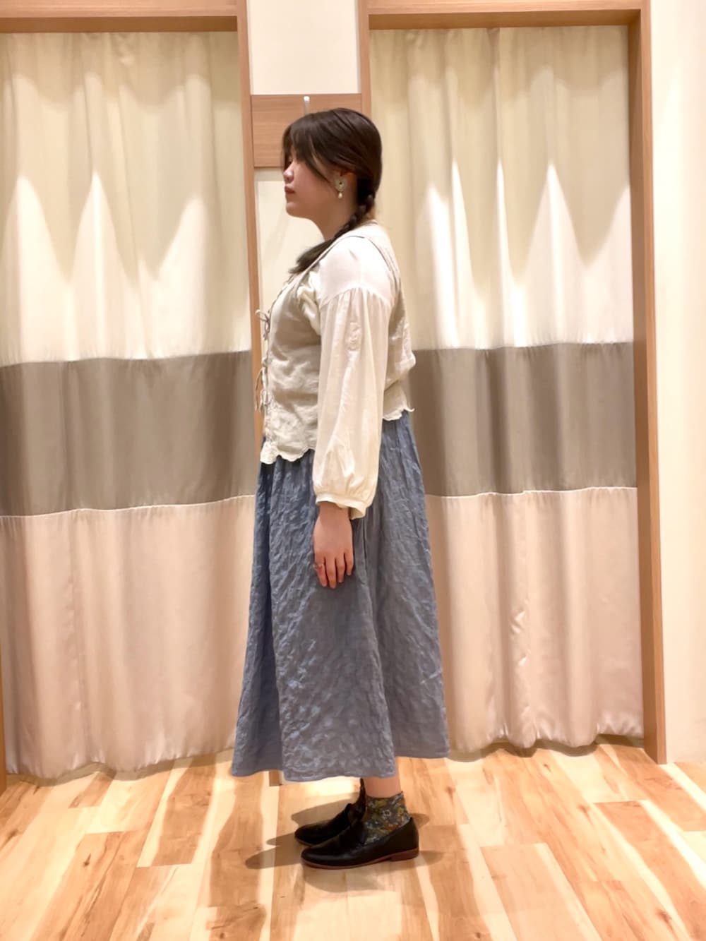 ブルー系のスカート、ベージュ系のベスト、ベージュ系のワンピースを着用したレディースの春コーディネートの3枚目の写真