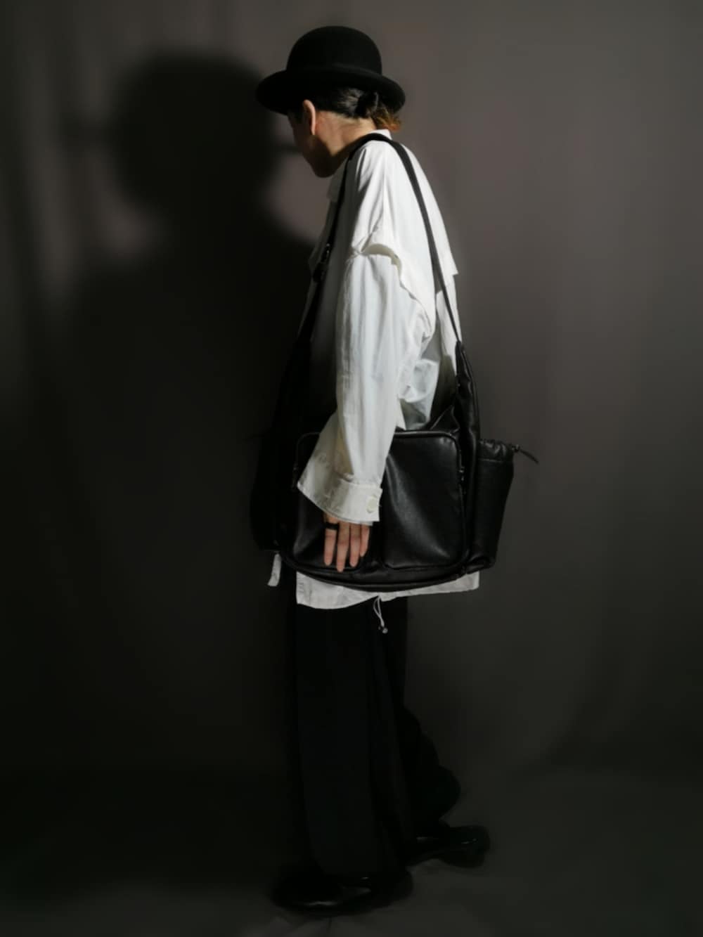 ブラック系のショルダーバッグ、ホワイト系のトレンチコート、ブラック系のサンダルを着用したメンズの秋コーディネートの2枚目の写真