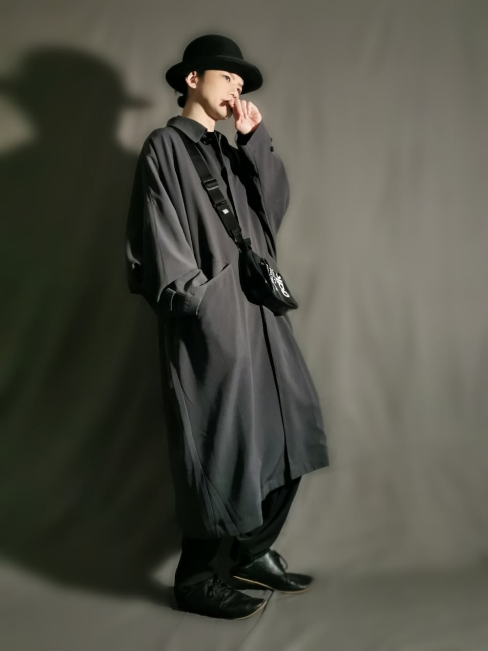 グレー系のステンカラーコート、ブラック系のショルダーバッグ、ブラック系のドレスシューズを着用したメンズの冬コーディネートの2枚目の写真