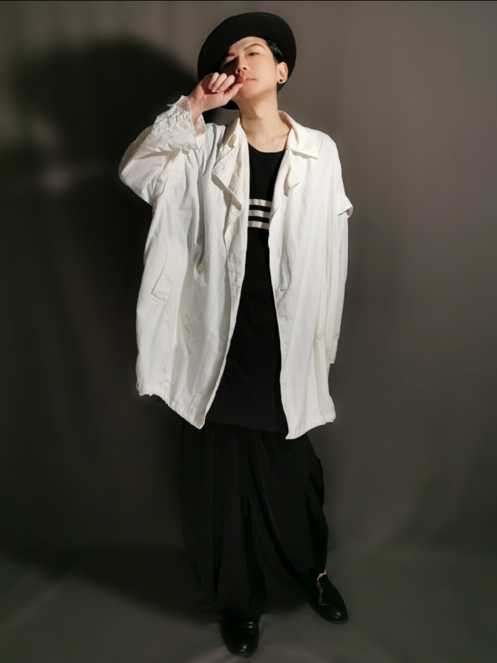 ブラック系のショルダーバッグ、ホワイト系のトレンチコート、ブラック系のサンダルを着用したメンズの秋コーディネートの3枚目の写真