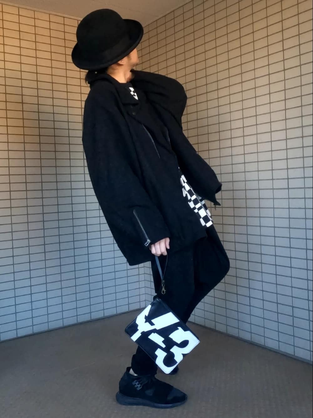 ブラック系のライダースジャケット、ブラック系のスニーカー、ブラック系のクラッチバッグを着用したメンズの冬コーディネートの2枚目の写真