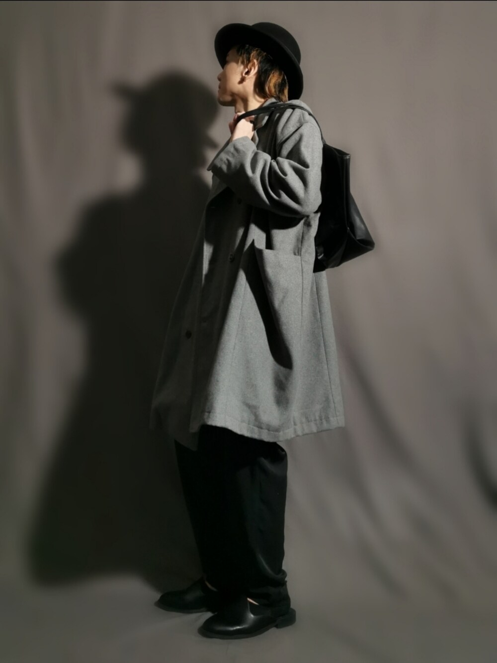 グレー系のチェスターコート、ブラック系のトートバッグ、ブラック系のパンツを着用したメンズの冬コーディネートの2枚目の写真